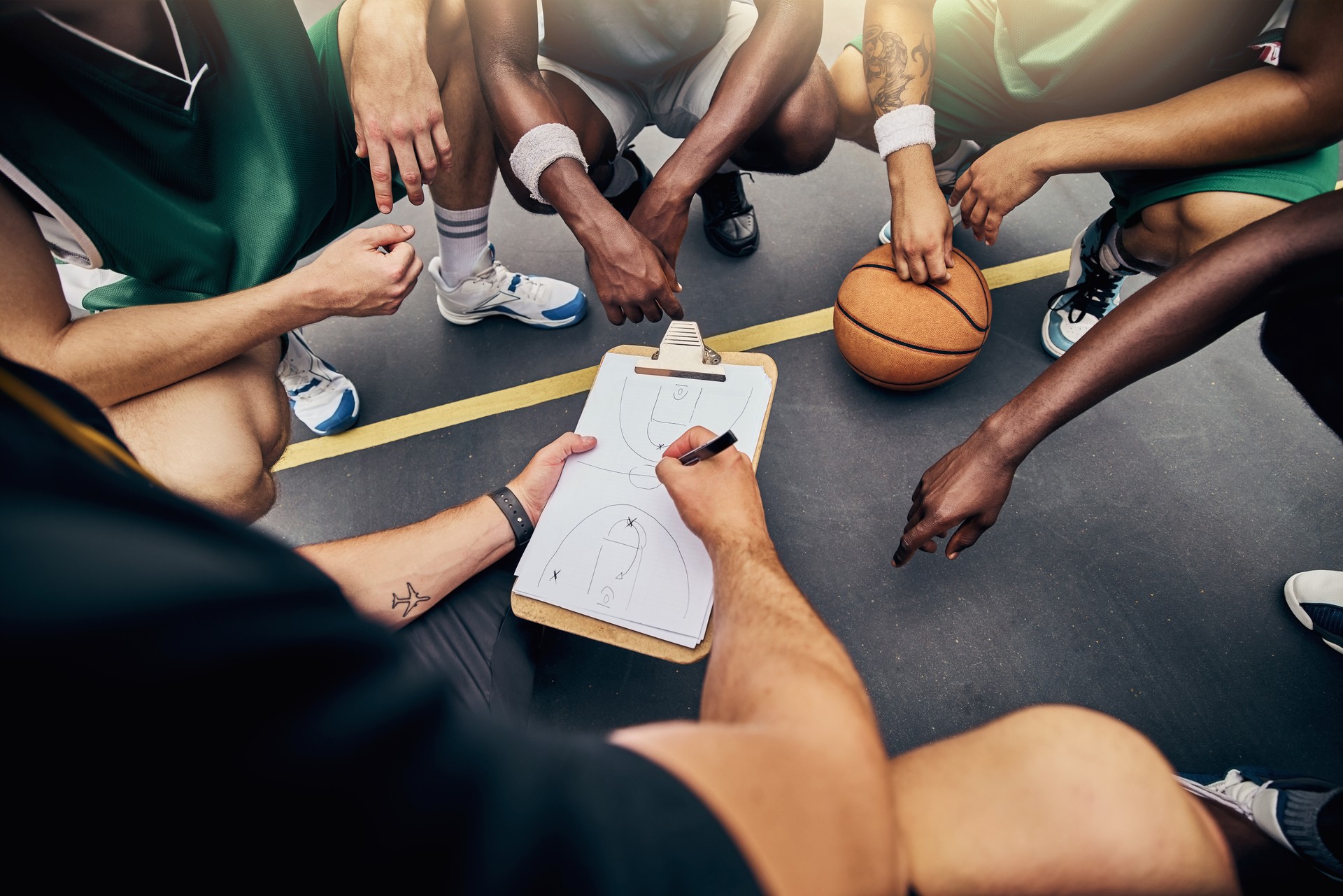 Basketball, strategy and team with a sports coach talking to a team while planning tactics on a clipboard and hands. Teamwork, fitness and exercise with a player and teammates listening at training